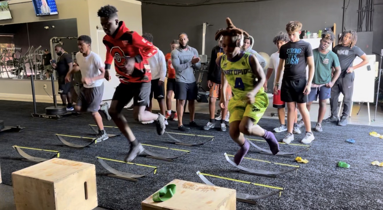 Youth athletes running agility drills over hurdles while coaches watch