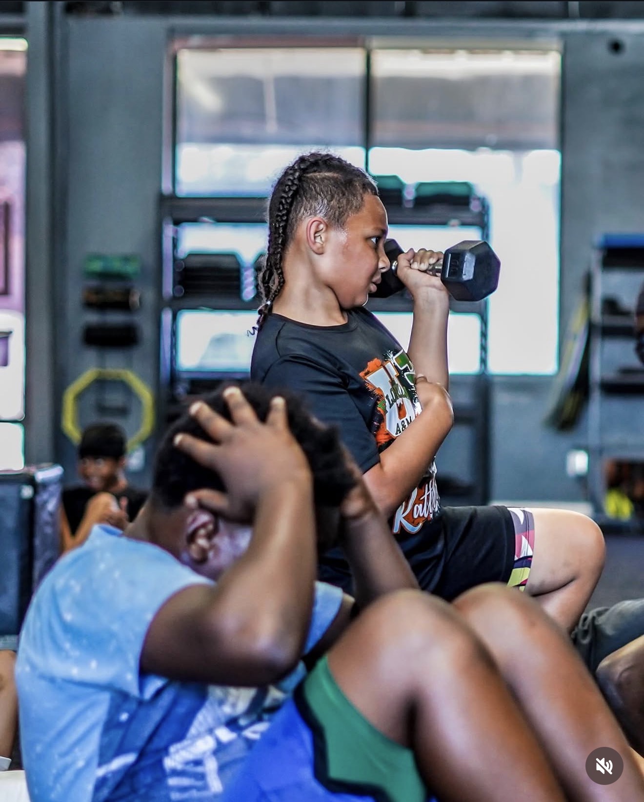 Young athlete pressing a dumbbell while teammates train nearby